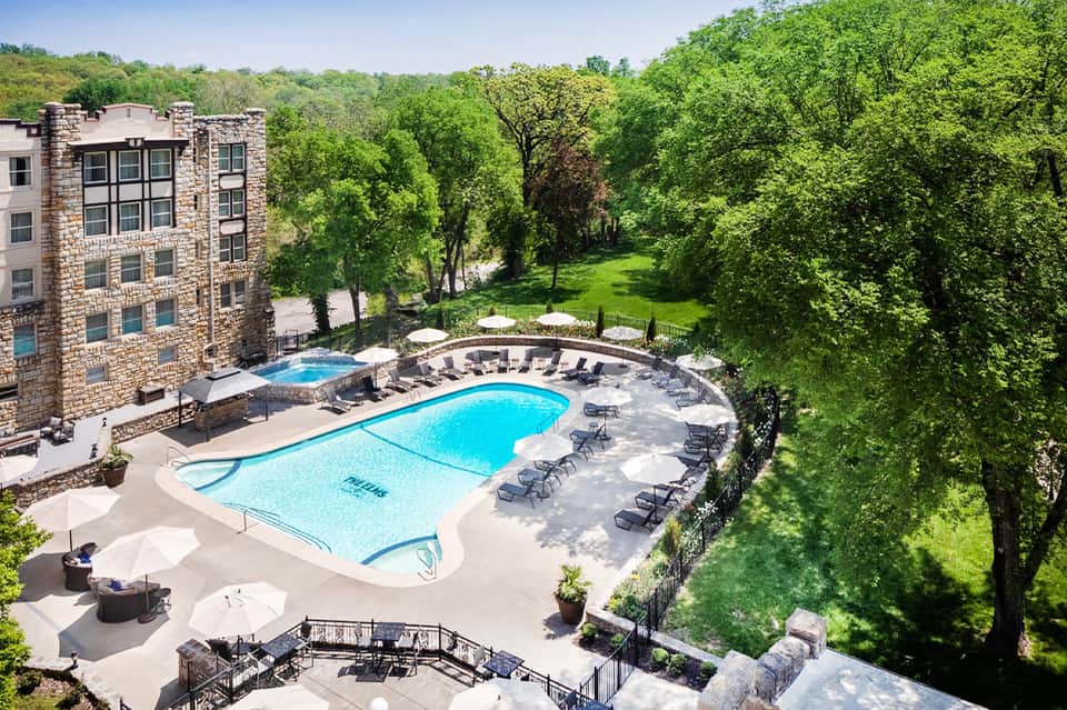 Aerial view of resort pool complex with stone building nestled in green wooded hillside