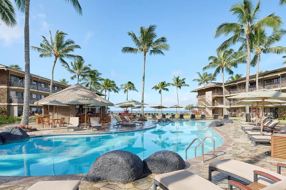 Resort pool with thatched-roof cabana, palm trees, and beachfront property at sunset