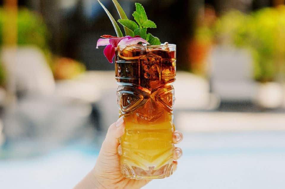 Hand holding a tropical cocktail with decorative rim and flower garnish, poolside setting