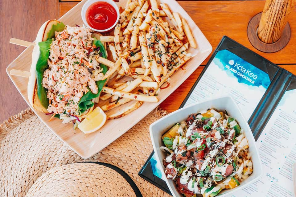 Seafood sandwich and loaded fries plated on wooden board at casual restaurant