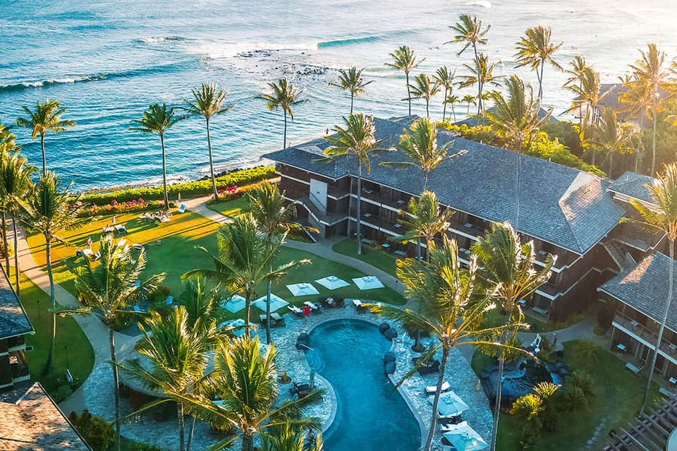 Aerial view of beachfront resort with curved pool, palm trees, and sandy beach access