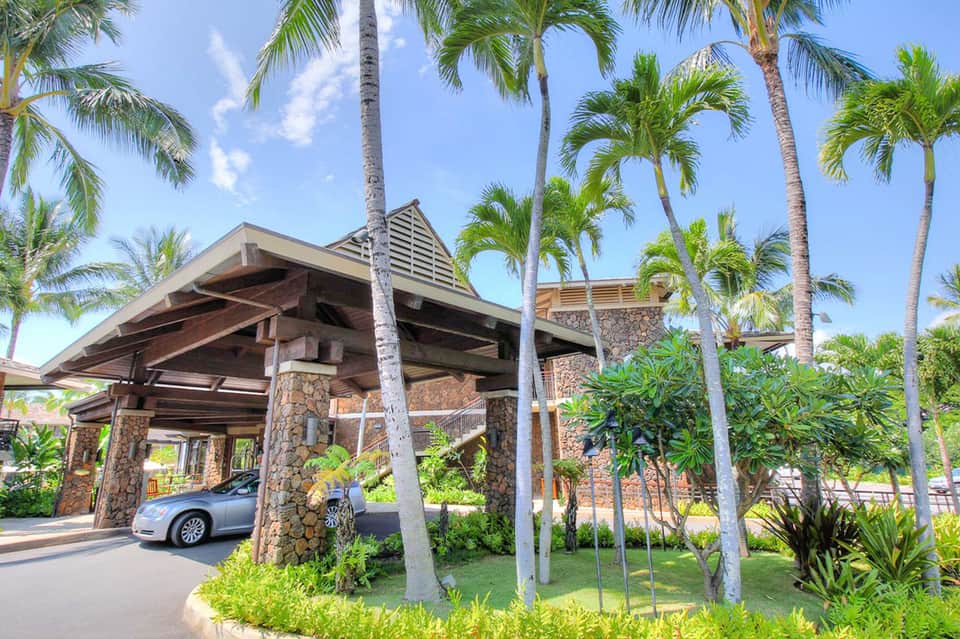 Modern resort entrance with stone pillars, carport, and tropical palm trees