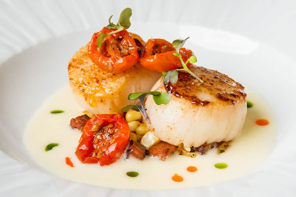 Elegantly plated seared scallops with roasted peppers and microgreens on white plate