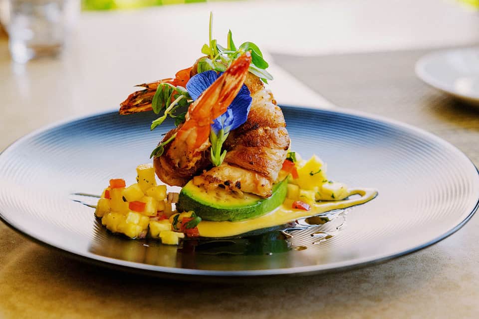 Elegantly plated seafood dish with vegetables and edible flowers on white ceramic plate