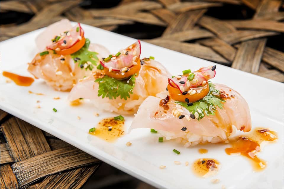 Plated sushi appetizers with fresh fish, sesame seeds, and colorful garnish on white plate