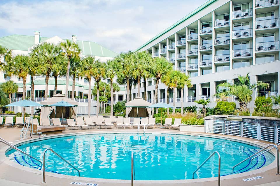 Circular swimming pool with lounge chairs and umbrellas in front of multi-story hotel
