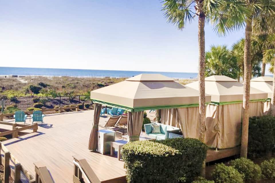 Beachfront patio with cabanas, cream-colored canopies, turquoise chairs, and ocean horizon view