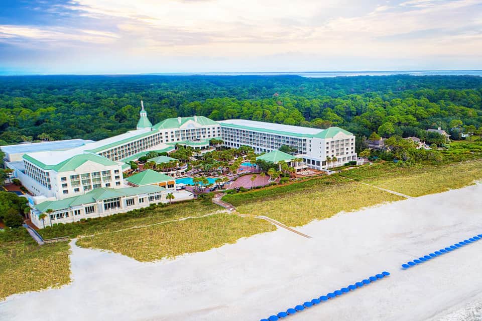 Aerial view of large resort with white and green roofing surrounded by lush tropical forest and airstrip