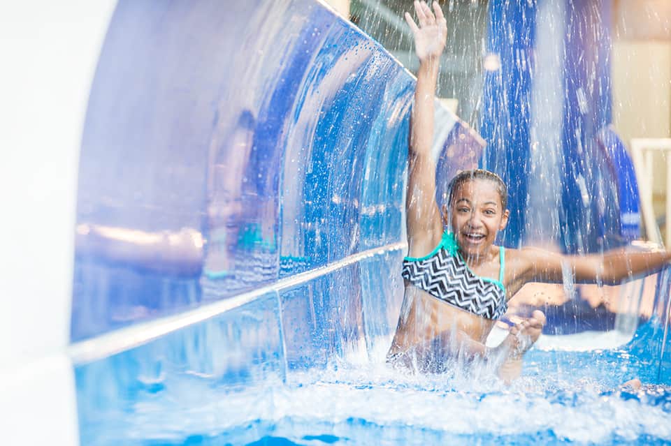 Child playing in water slide with cascading water at indoor pool facility