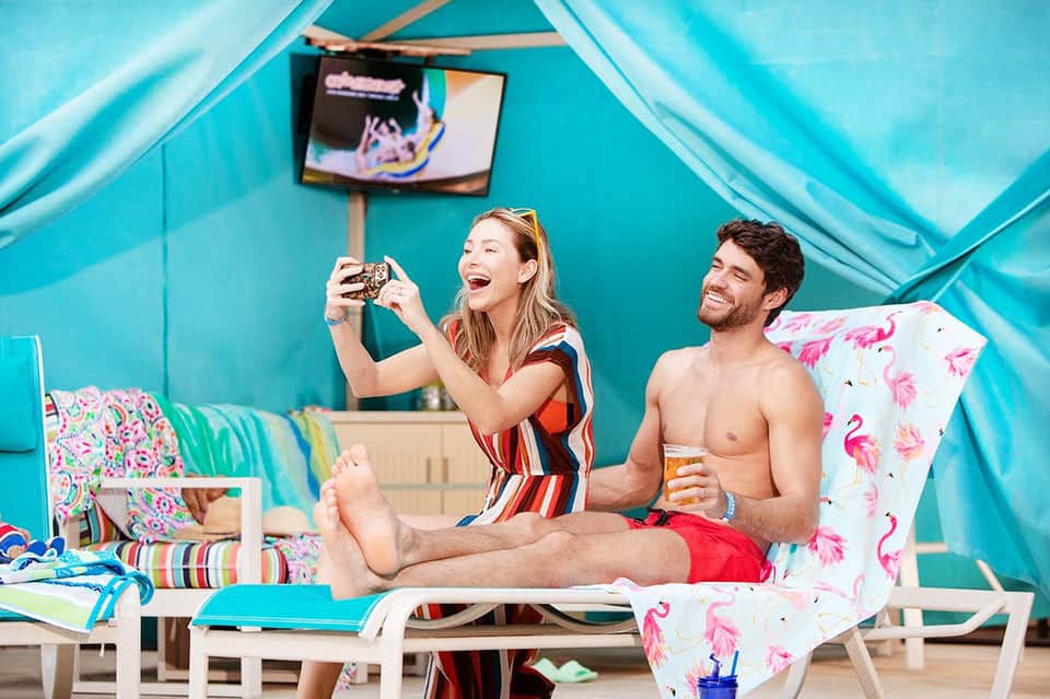 Couple in cabana taking selfie with turquoise tent ceiling and poolside decor