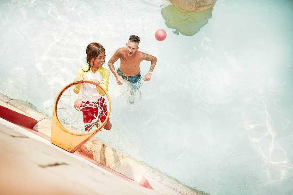 Father and daughter playing basketball in shallow turquoise resort pool water