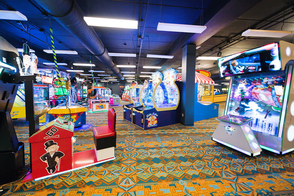 Indoor arcade game room with colorful machines, bright lighting, and patterned carpet