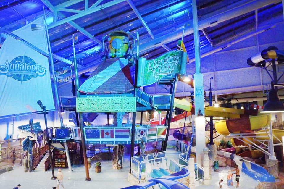 Indoor water park with Aquatopia and Karuttes Quest rides under blue-lit glass ceiling