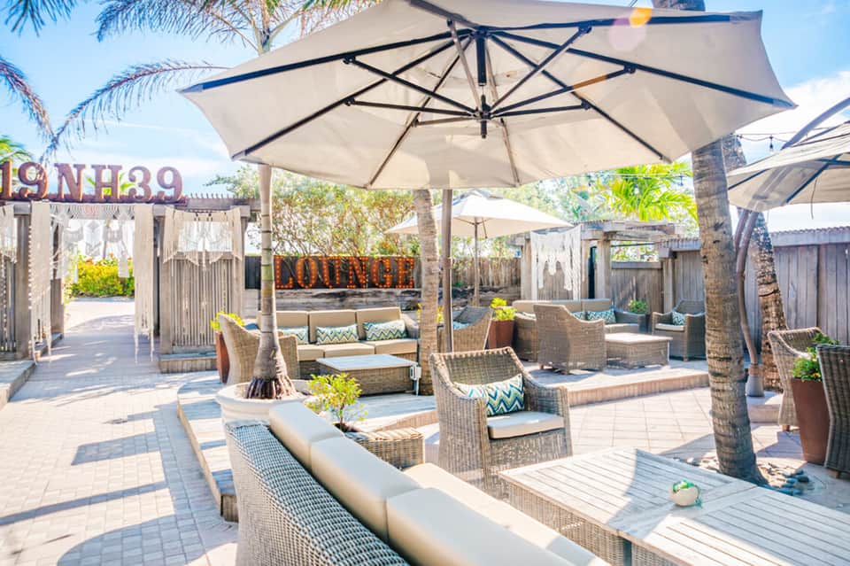 Upscale poolside lounge with large umbrellas, woven furniture, cushioned seating, and tropical landscaping