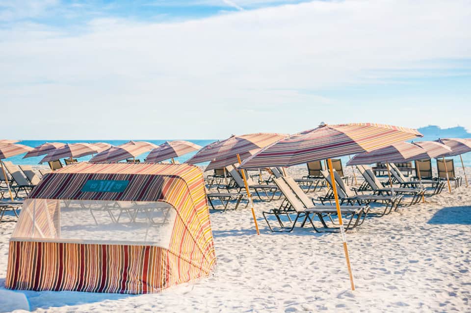 Sandy beach lined with colorful striped umbrellas and lounge chairs under blue sky