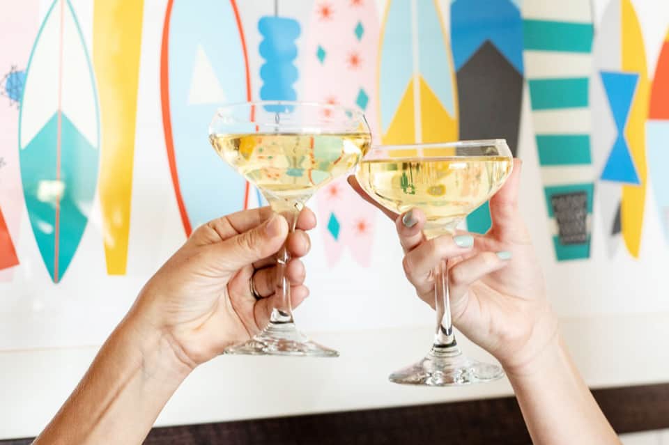 Two hands toasting with champagne glasses against colorful geometric party backdrop