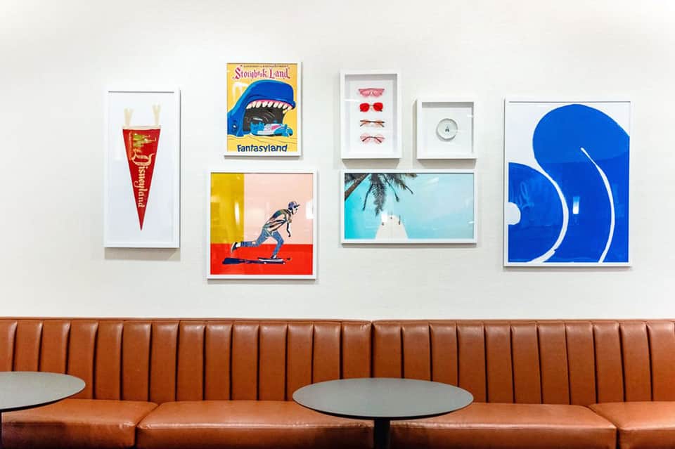 Interior wall displaying framed vintage artwork and memorabilia, with an orange leather booth seating below.