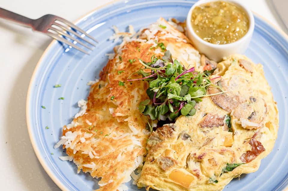 Omelet with hash browns, garnished with microgreens and served with sauce on blue-rimmed plate