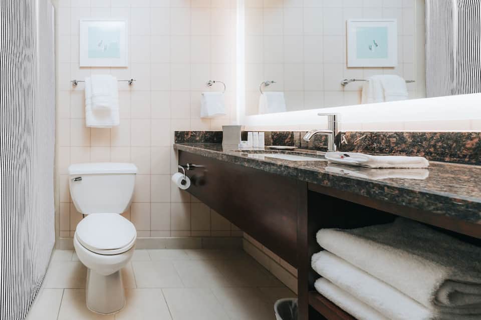 Clean hotel bathroom with white tile, double sink vanity, toilet, and white towels