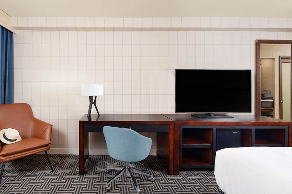 Hotel room with white tiled walls, desk, flat-screen TV, and mid-century modern furnishings