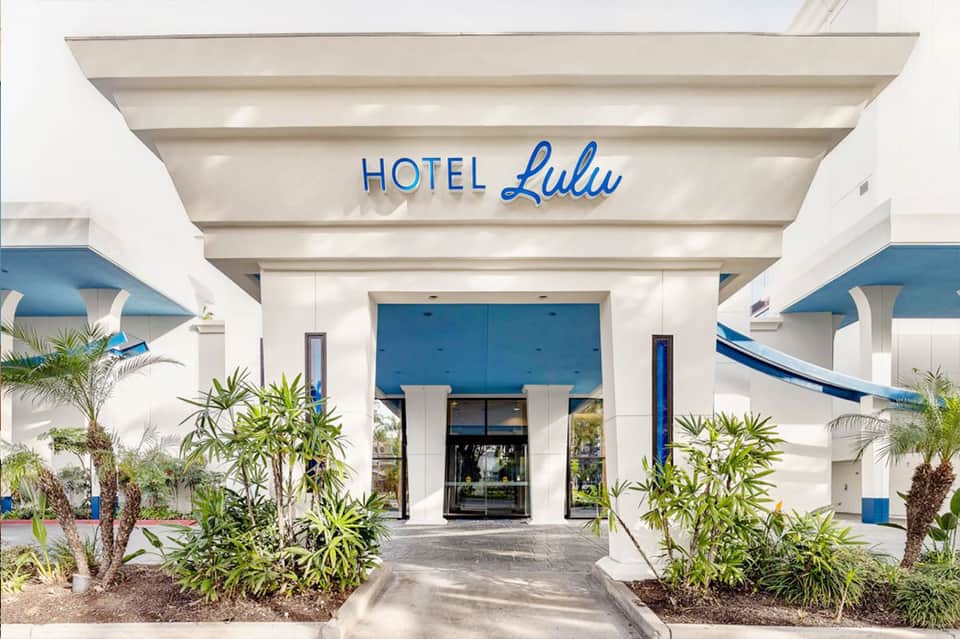 Modern white hotel entrance with blue accents, palm landscaping, and Hotel Lulu signage