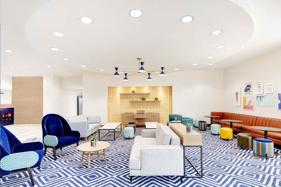 Contemporary lobby lounge with patterned rug, blue velvet chair, cream sofas, and modern pendant light