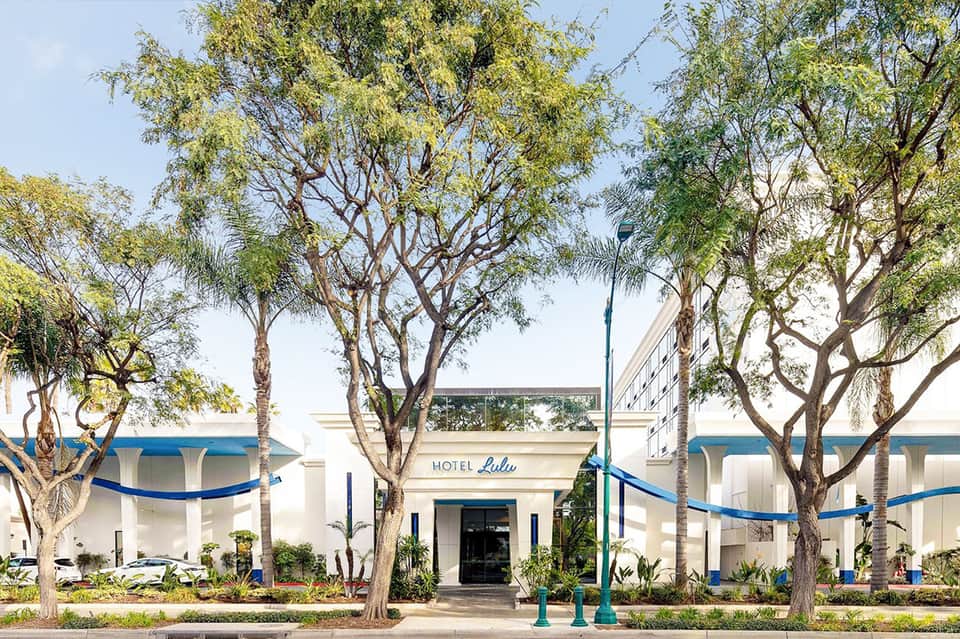 Historic Hotel Lulu entrance with white building, blue trim, and mature palm trees along streetfront