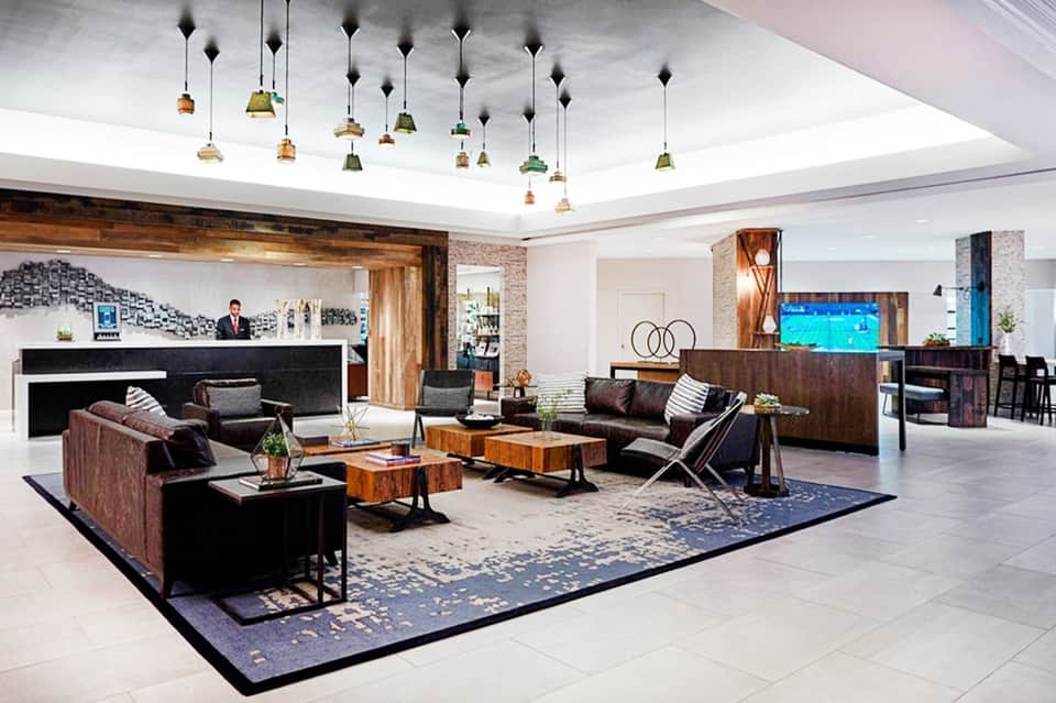 Contemporary hotel lobby with modern furnishings, pendant lights, fireplace, and dark wood accents