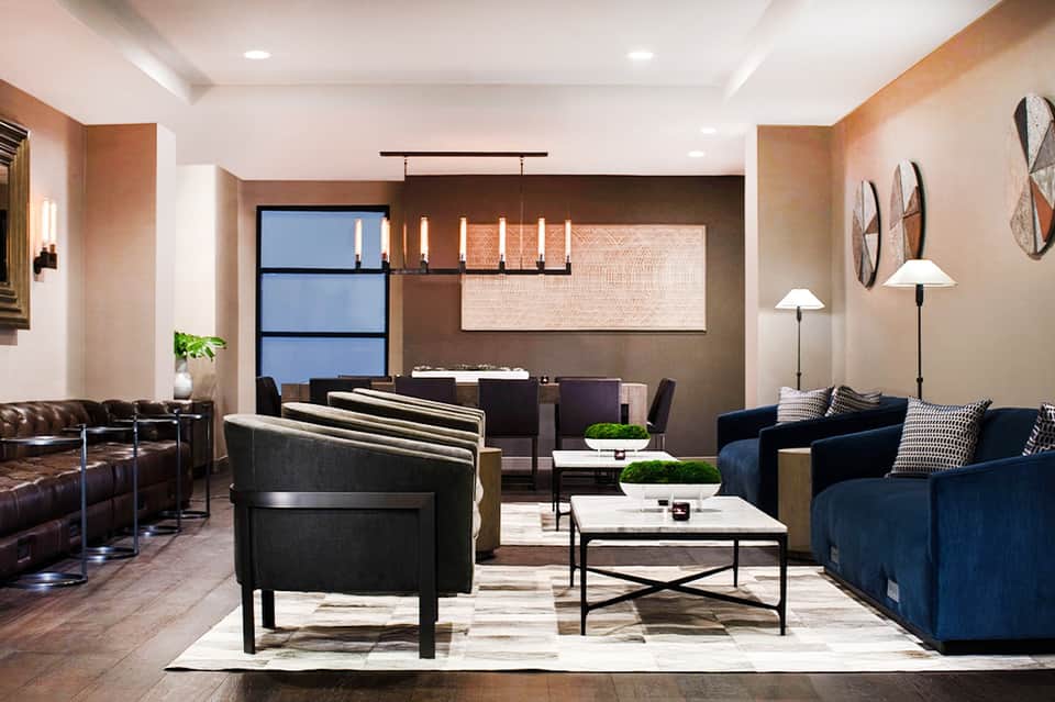 Elegant hotel lobby lounge with navy and tan seating, pendant lighting, and warm earth tones