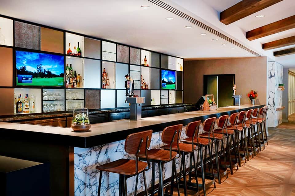Sophisticated hotel bar with marble countertop, brown leather chairs, and illuminated bottle display wall