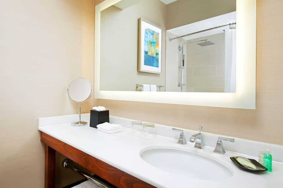 Modern bathroom with large illuminated mirror, white countertop, and chrome fixtures