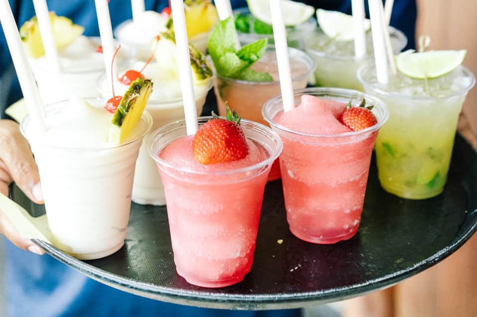 Colorful cocktails with fruit garnishes served on a black tray with white straws