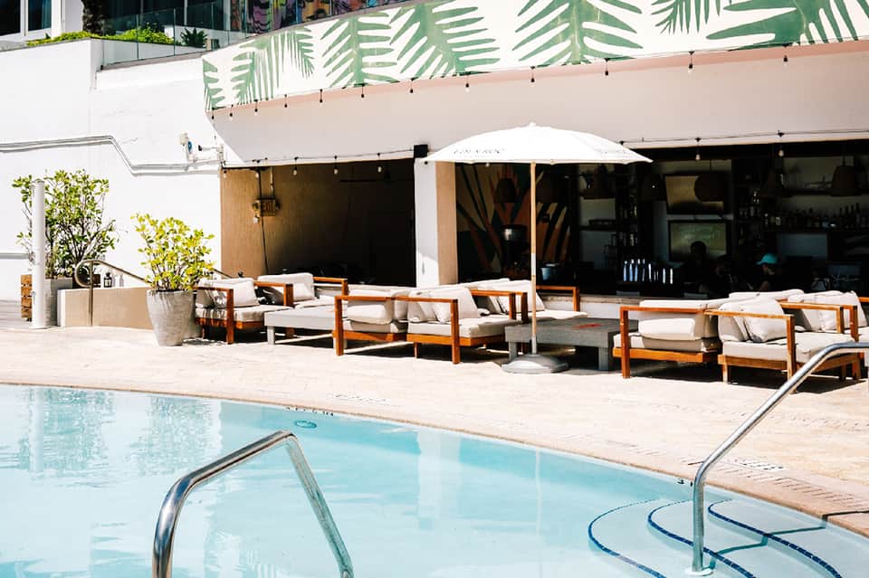 Modern poolside lounge with wooden furniture, white umbrella, and tropical foliage backdrop