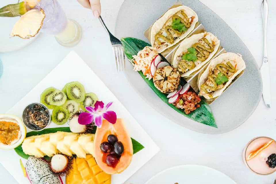 Gourmet tropical dishes including grilled shrimp buns, fresh fruit, and seafood platter