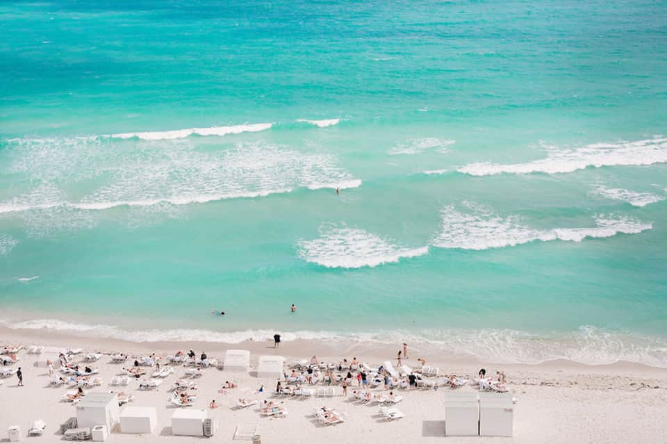Overhead view of crowded beach with turquoise ocean waves and white beach cabanas