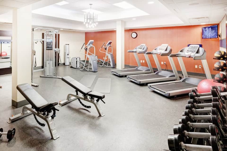 Modern fitness center with treadmills, ellipticals, and weight equipment against orange wall
