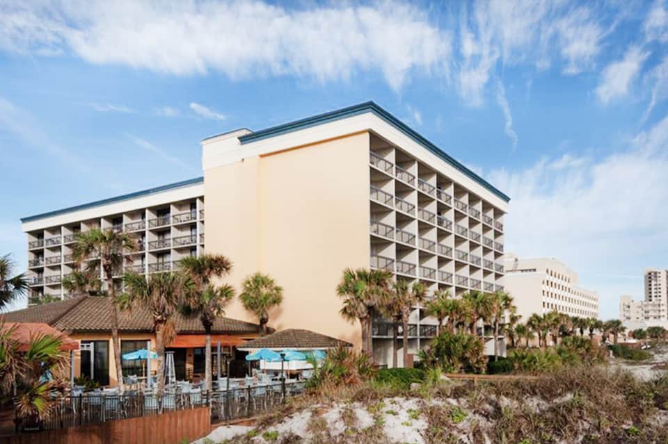 Beachfront hotel resort with multi-story building, palm trees, and blue umbrellas on sand