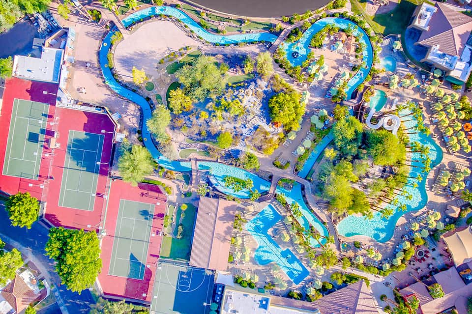 Aerial view of resort with winding lazy river, water slides, tennis courts, and lush landscaping