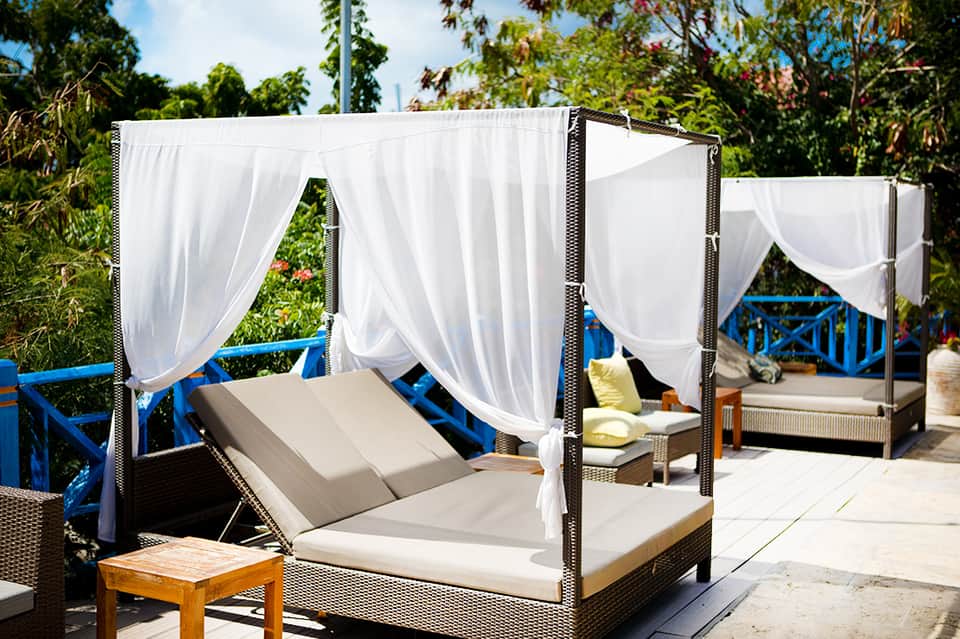 Outdoor cabana beds with white curtains overlooking resort pool and tropical vegetation