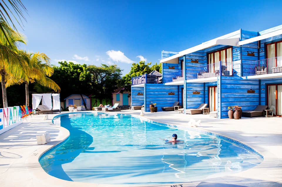 Bright blue pool with modern cabanas and palm trees under clear blue sky