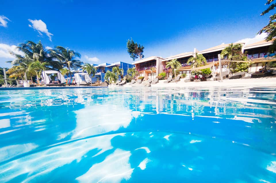 Crystal-clear resort pool with colorful loungers and palm-lined buildings