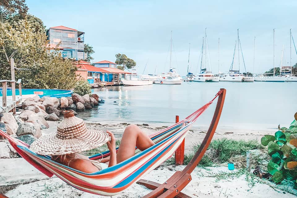 Beachfront hammock with sailboats anchored in turquoise bay and colorful boat houses