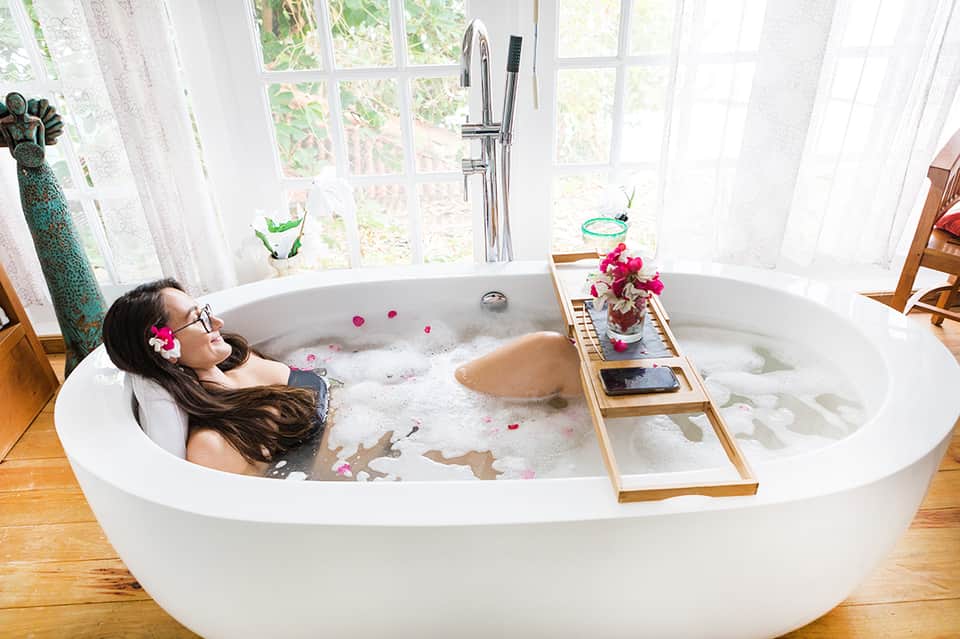 Woman relaxing in luxurious freestanding bathtub filled with flower petals overlooking green gardens