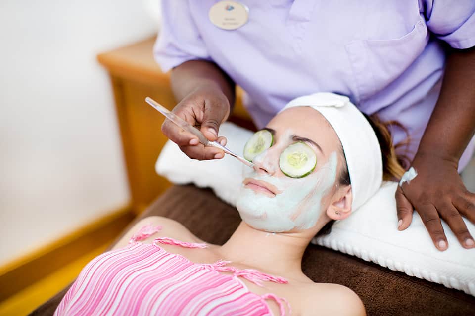 Spa therapist applying facial mask to client with cucumber slices