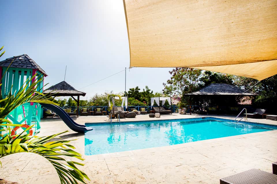 Resort swimming pool with slide, shade structures, and lounge seating during daytime