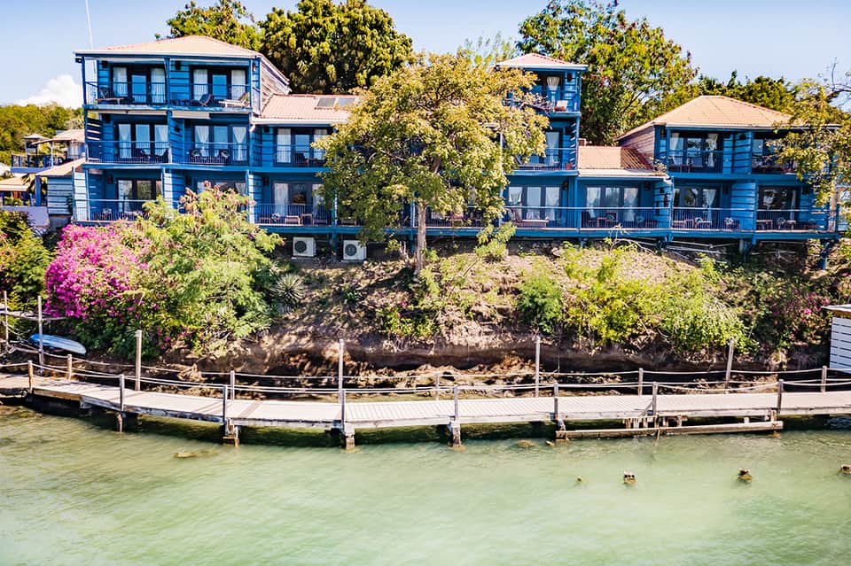 Blue waterfront homes with multiple stories and decks overlooking green water and vegetation