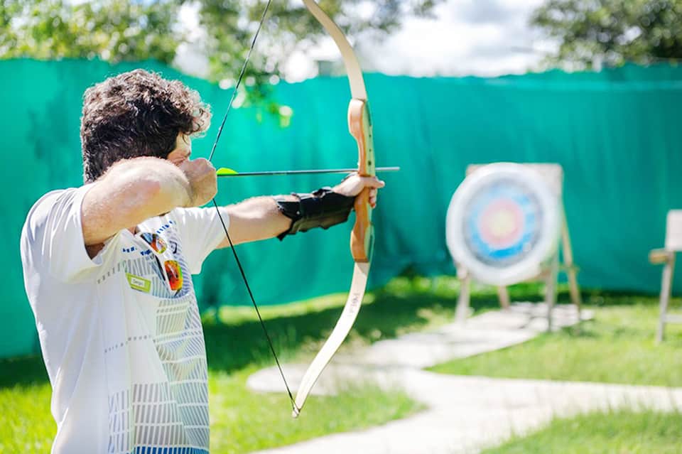 Man practicing archery outdoors with target and green safety barrier