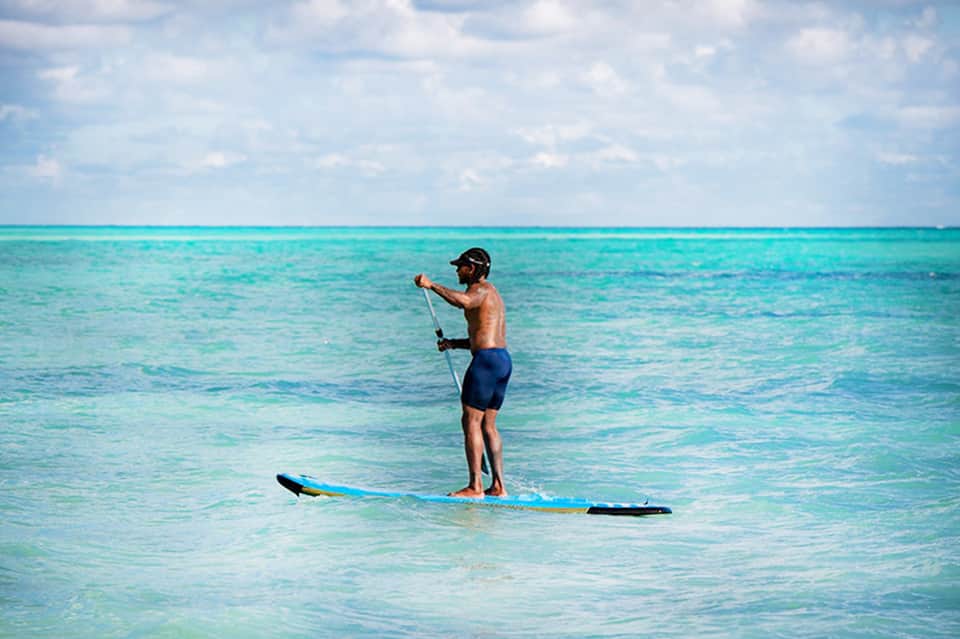Man stand-up paddleboarding on turquoise water with clear blue sky and clouds