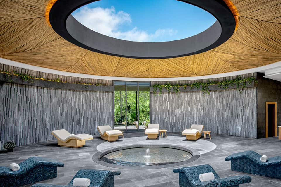 Modern spa lounge with circular hot tub, loungers, and geometric wooden ceiling