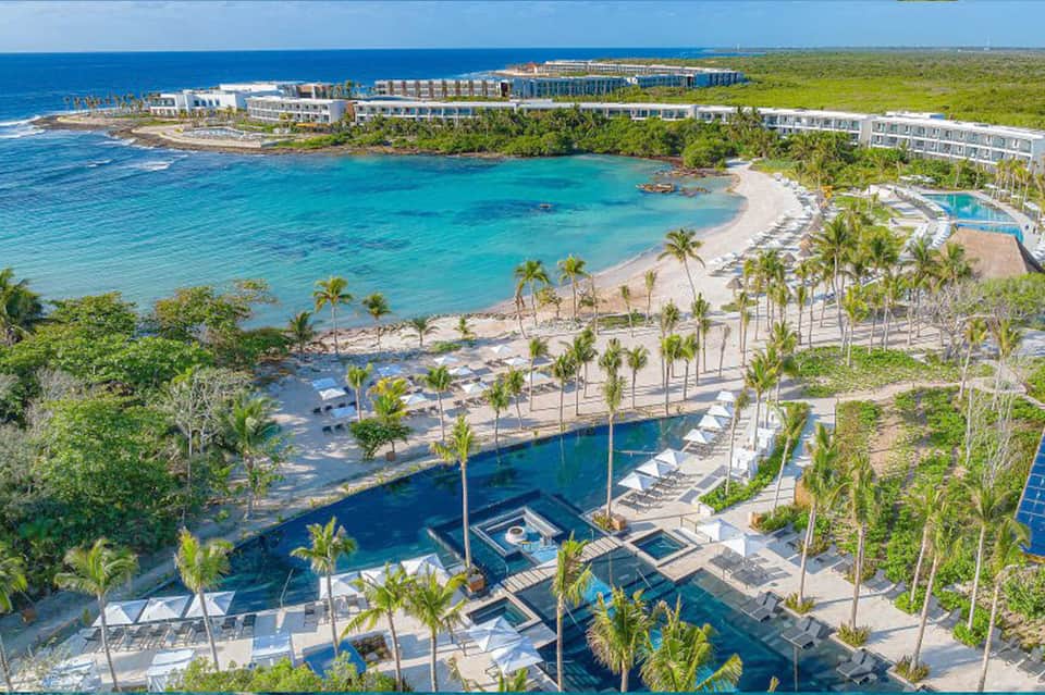 Aerial view of beachfront resort with turquoise pools, palm trees, white sand beach, and ocean